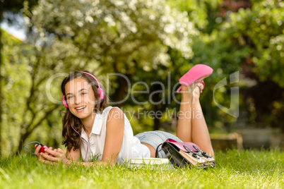 Laughing student girl with headphones lying grass