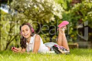 Laughing student girl with headphones lying grass