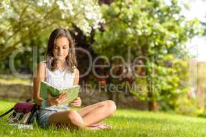 Student girl reading book sitting on grass