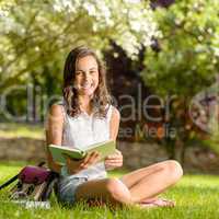 Cheerful girl with open book sitting grass
