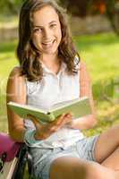 Cheerful student girl sitting grass read book