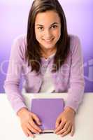 Smiling student girl sitting behind desk purple