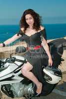 Model on a motorcycle with helmet in hand against the sea