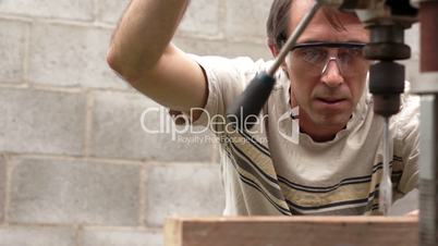 Man Using Drill Press On Wood Board