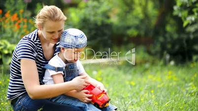 Boy playing with toy car sitting on moms lap outdoor