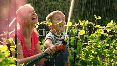 Mother helping son to water the garden with hose