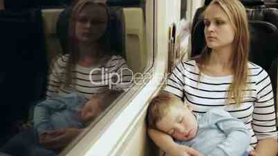 Tired woman in the train with sleeping son on her lap