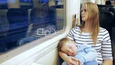 Woman looking out the train window with her son sleeping on lap