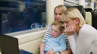 Family with child in the train watching video on laptop