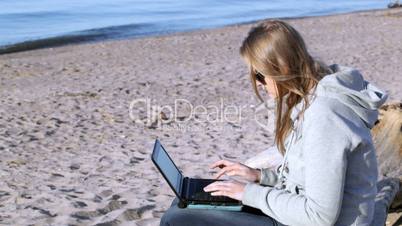 Woman in sunglasses using laptop on the beach