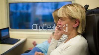 Woman in the train having a phone talk. Mother and son watching video