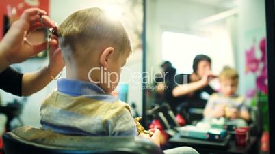 Hairdresser cutting childs hair while he playing with a toy