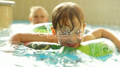 Happy little boy swimming with rubber ring in the pool