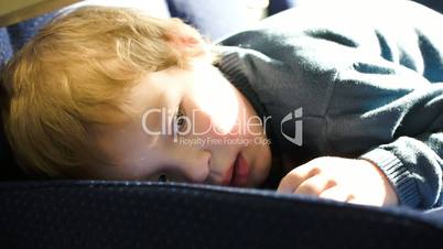 Little boy lying on the seat in bus, car ot train