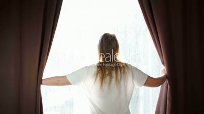 Woman opening curtains and stretching out in the morning