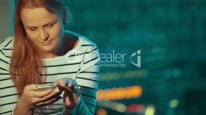 Woman using phone sitting by window in the evening