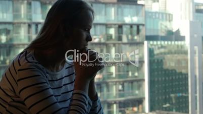 Sad woman being deep in thoughts and then looking out the window with city view