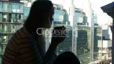Woman at the window with mug looking city modern glass building