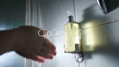 Hands pushing a container with soap under shower stream