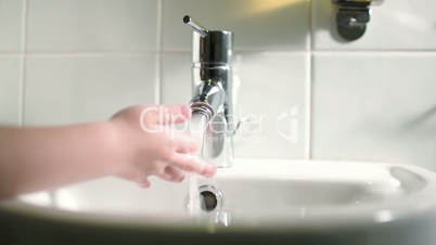 Childs hand touching water pouring from tap