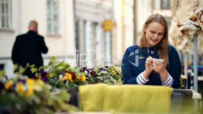 Woman using her smartphone sitting in outdoor cafe