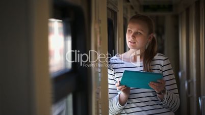 Young woman with pad standing by the window in train hallway