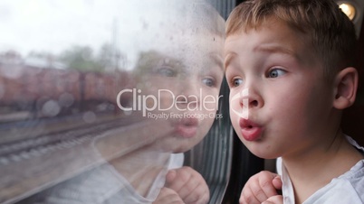 Curious boy looking out of the train window in rainy weather