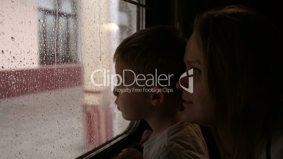 Mother and son in train looking out the window on a rainy day