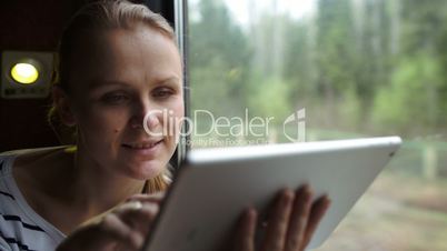 Young woman using touch pad sitting by the window in train