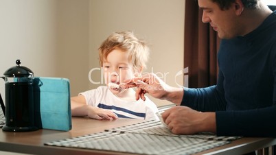 Father feeding his son while he watching cartoons on pad