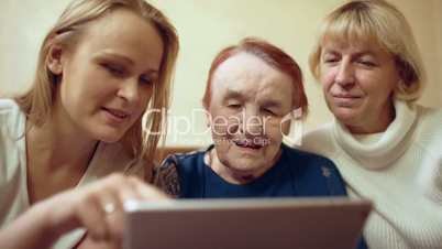 Woman with pad showing photos or video to her mother and grandmother