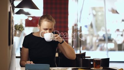 Young woman sitting in cafe with pad and drinking coffee