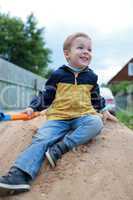 Happy little boy sitting on sand hill