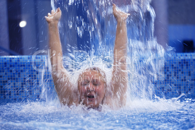 Woman under water stream in the swimming pool