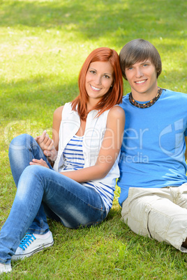 Teenage couple sitting on grass embracing summer