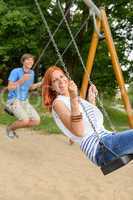 Laughing teenage couple on swing in park