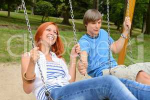 Cheerful teenage couple on swing in park