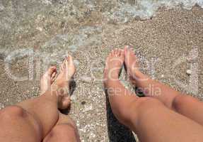 Legs of a man and a woman with her feet in the sea
