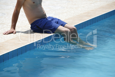 Attractive man with blue swimsuit sitting on the edge of the poo
