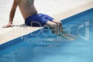 Attractive man with blue swimsuit sitting on the edge of the poo