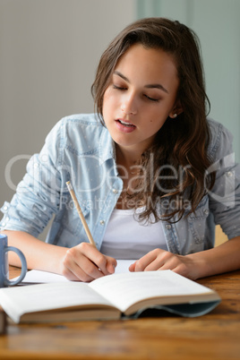 Teenage girl studying book writing notes