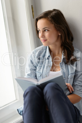 Teenage girl sitting with book by window