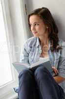 Teenage girl sitting with book by window
