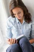 Teenage girl reading book sitting by window
