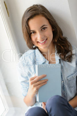 Teenage girl sitting by window hold book