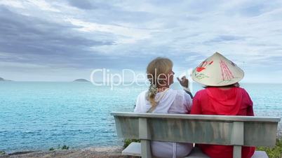 Two women sitting on a bench talking at the sea