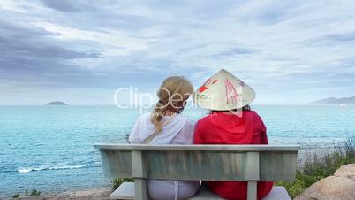Two women sitting on a bench talking at the sea