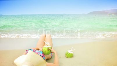 Young woman in swimsuit with coconut cocktail on the beach.