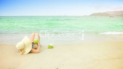 Young woman in swimsuit with coconut cocktail on the beach.