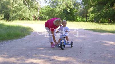 Grandmother assisting child to ride a bicycle in summer park